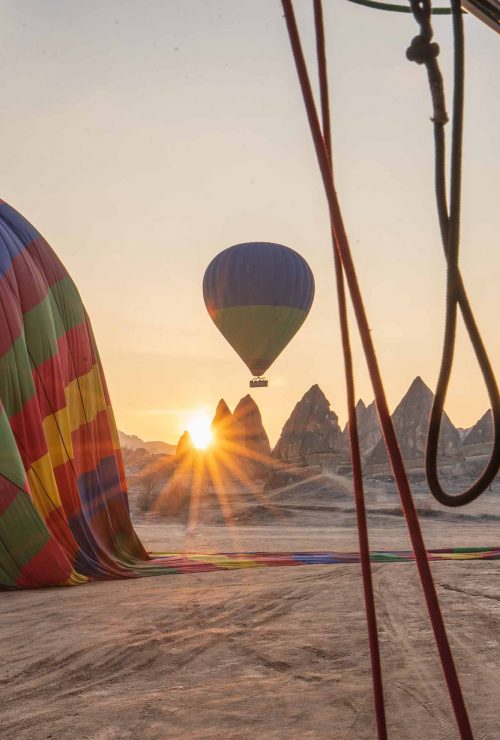 In Kappadokien geht über den Feenkaminen die Sonne auf, während die Heißluftballone landen.